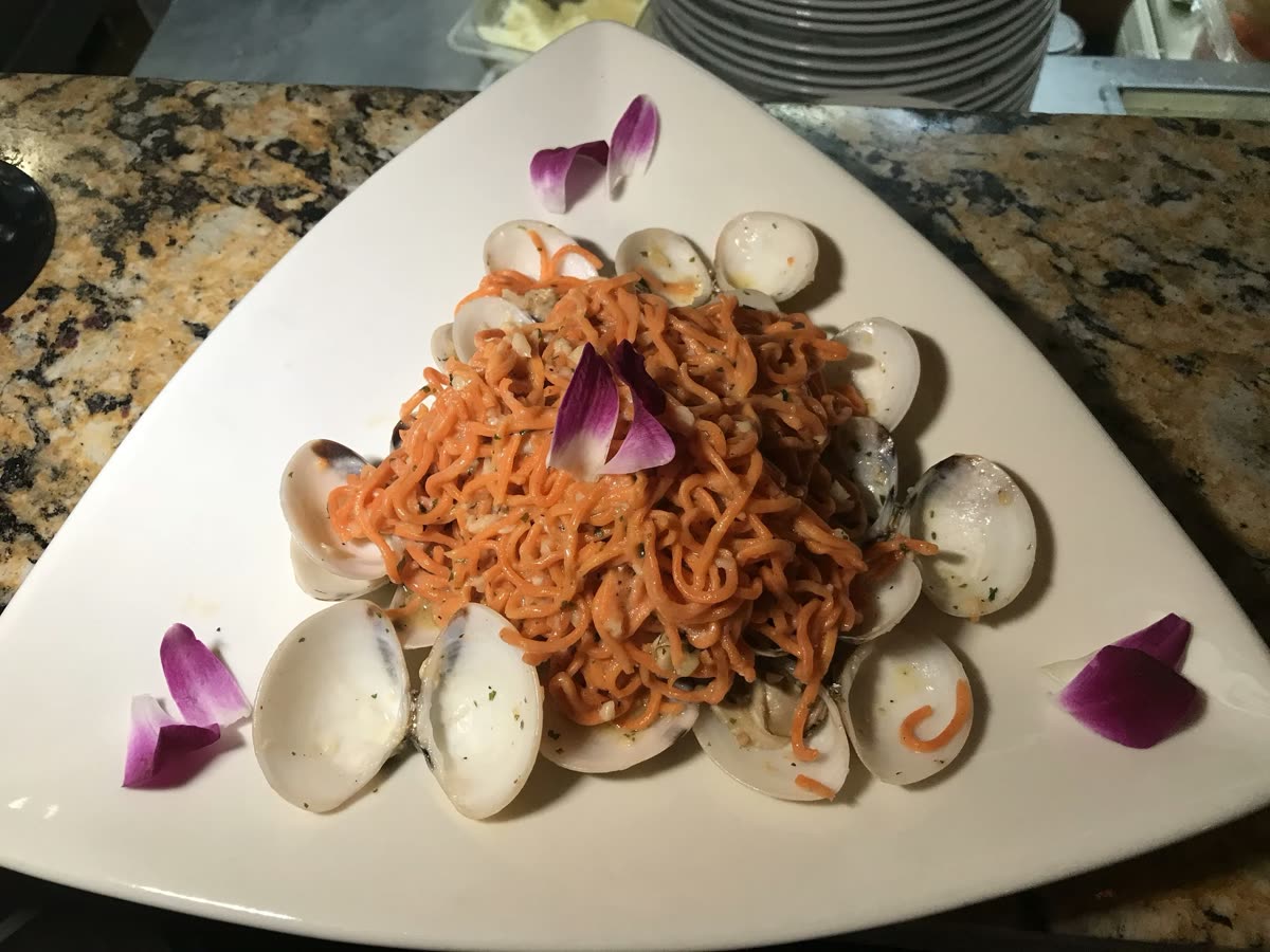 Red-sauce pasta piled over fresh clams on a white plate