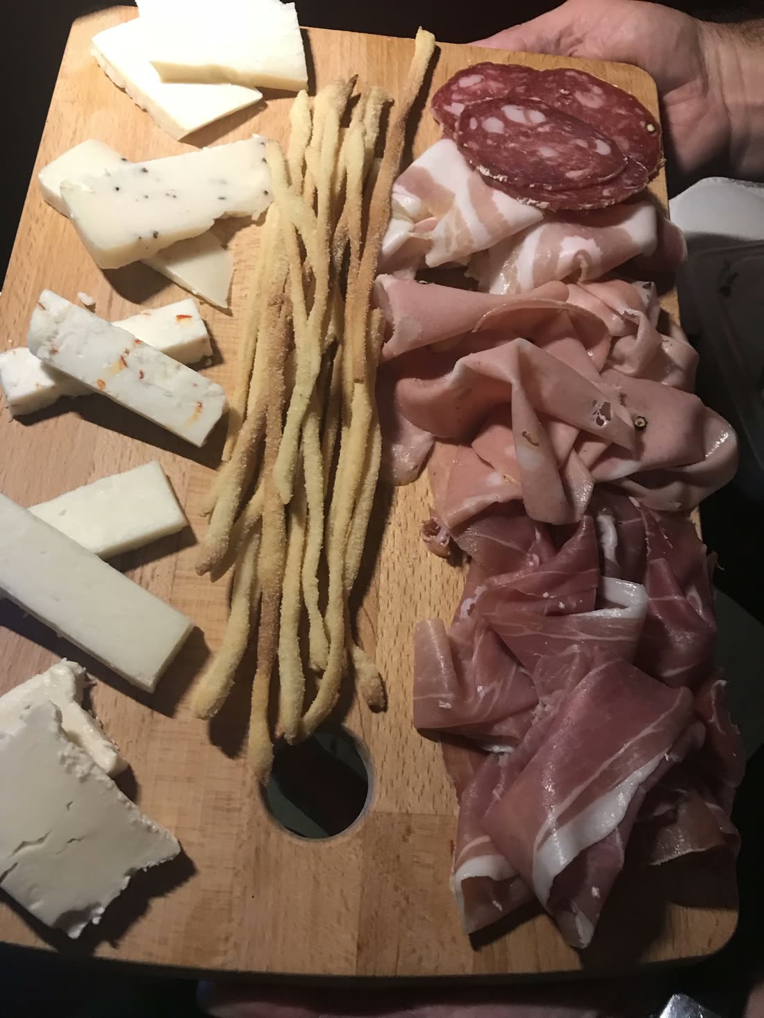 A wooden board of Italian salumi, cheeses and grissini held up for the table